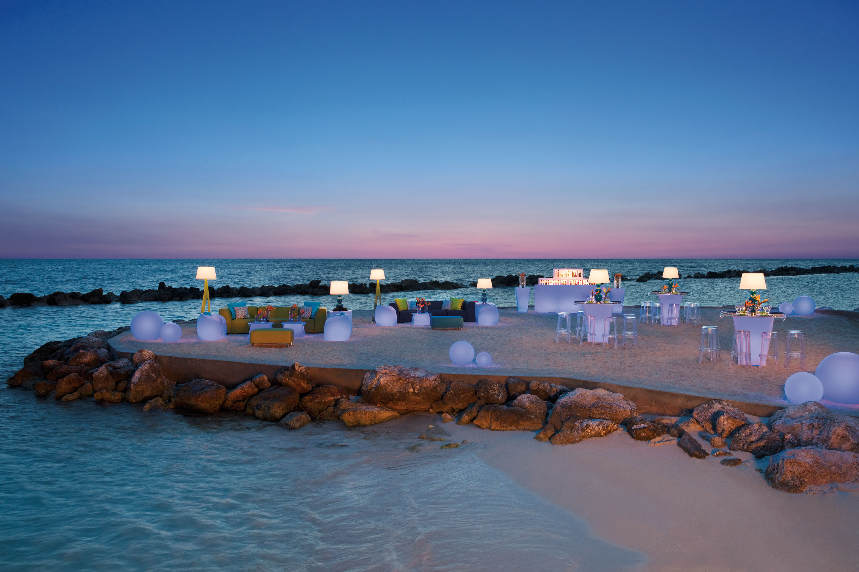 Elevated beach area set up with modern sitting areas, high top tables and bar at sunset